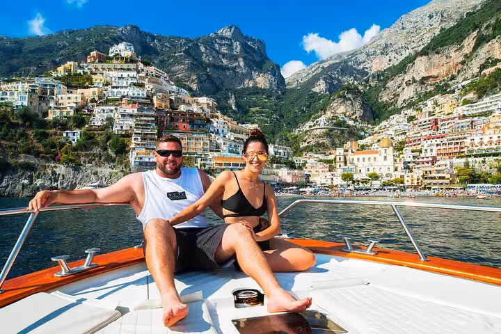 Smiling couple on a private boat tour, admiring Positano's stunning coastal views aboard a Gozzo 750.