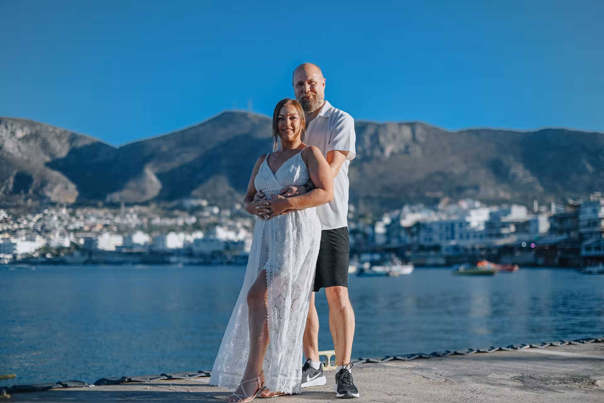 Couple enjoying a private photoshoot at the scenic Port of Hersonissos with mountains and sea in the background.