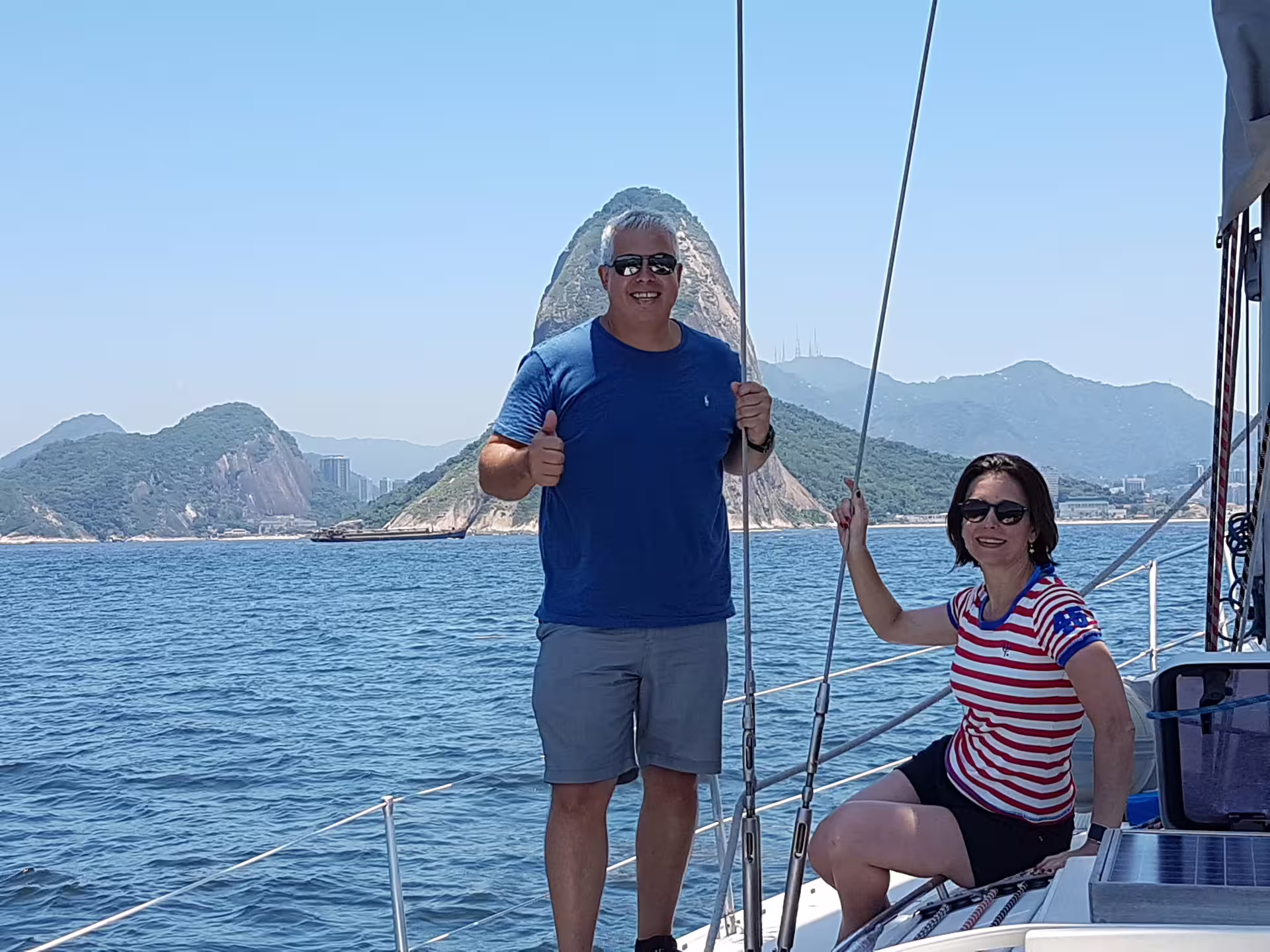 Couple smiling aboard a private sailing tour with stunning coastal views and clear blue skies.