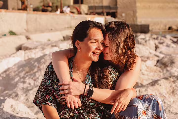 Couple embracing and smiling on a sunlit rocky beach in Naples, captured during a professional photography session.