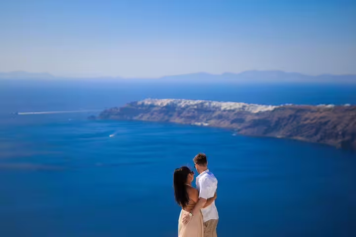 Couple embracing with panoramic Santorini caldera and blue Aegean backdrop, romantic proposal photo session