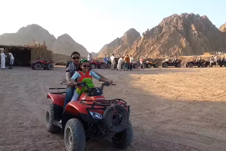Couple on a private Sharm El Sheikh quad bike tour, posing on ATV in Sinai desert camp with mountains behind