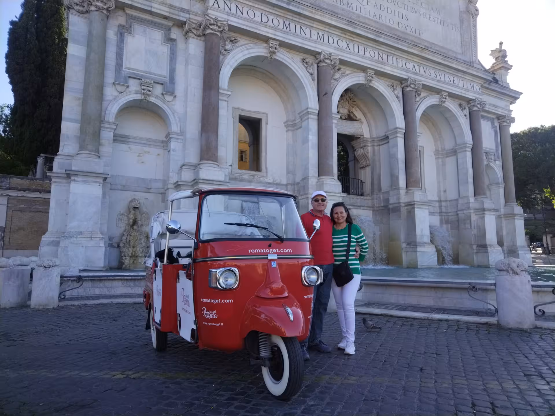 Couple posing with a red tuk-tuk in front of a historic Roman fountain, highlighting cultural city exploration.