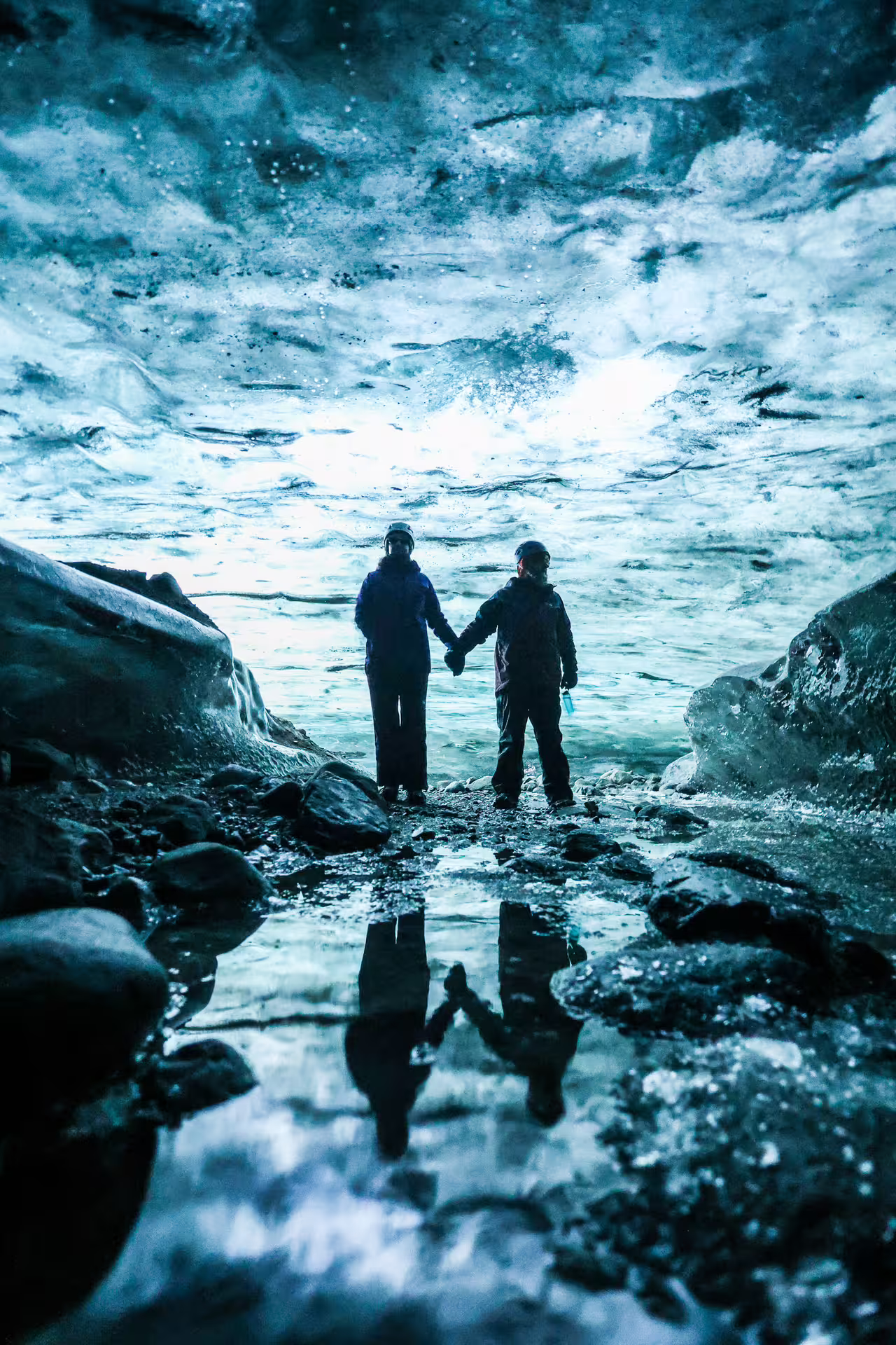 A couple holding hands reflected in still water inside a breathtaking crystal ice cave on Vatnajokull Glacier