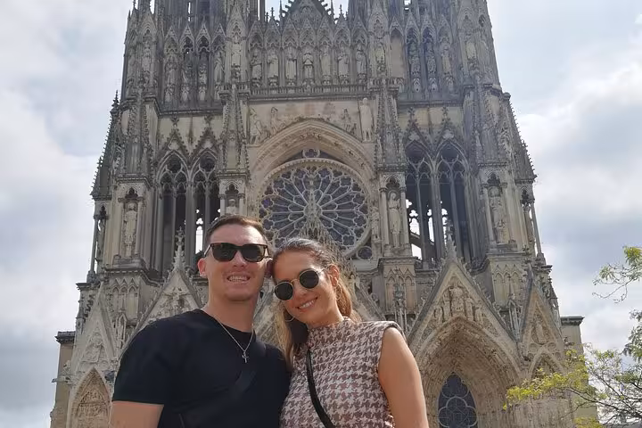Couple smiling in front of Reims Cathedral on a guided tour of Reims, France
