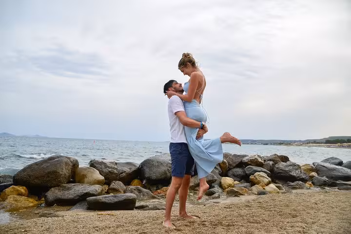 Couple joyfully embracing on a rocky beach with the ocean in the background during a romantic photoshoot in Malia.