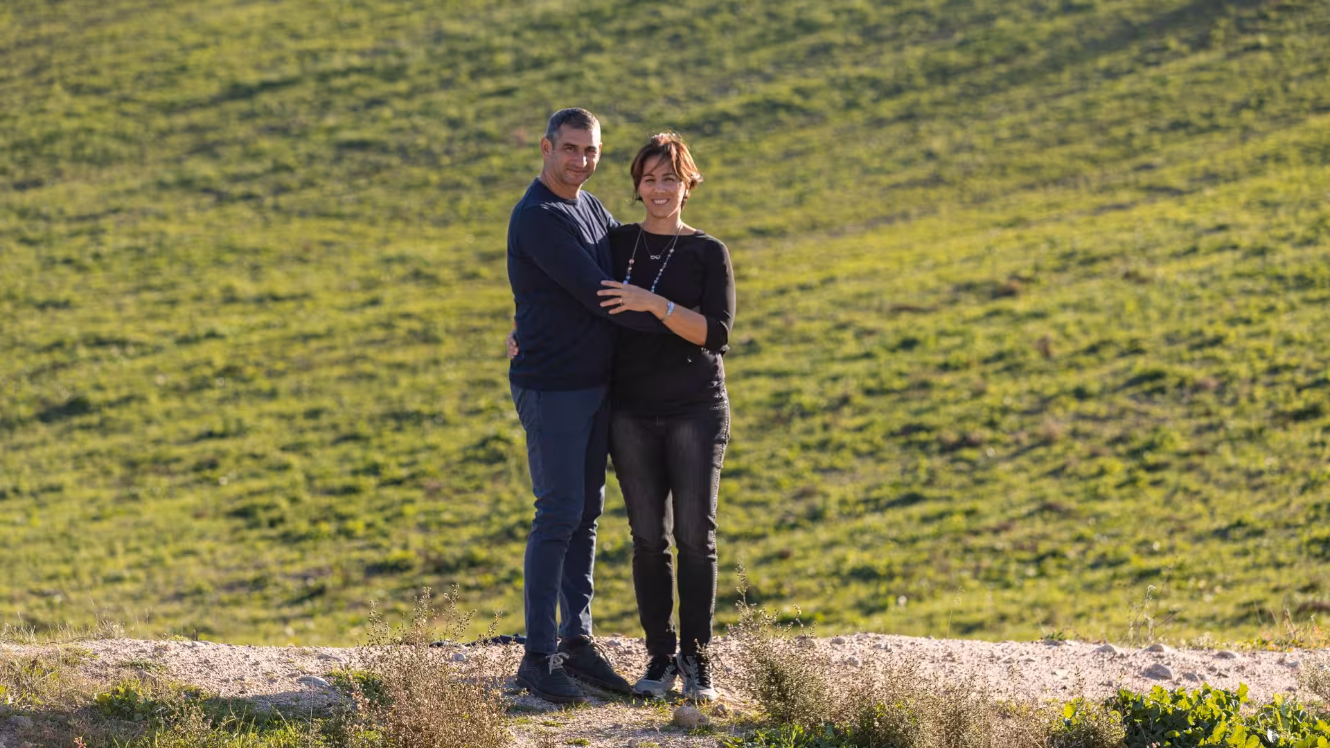A couple smiling in a lush green field in Tula, ideal for a romantic jam tasting getaway in Ozieri.