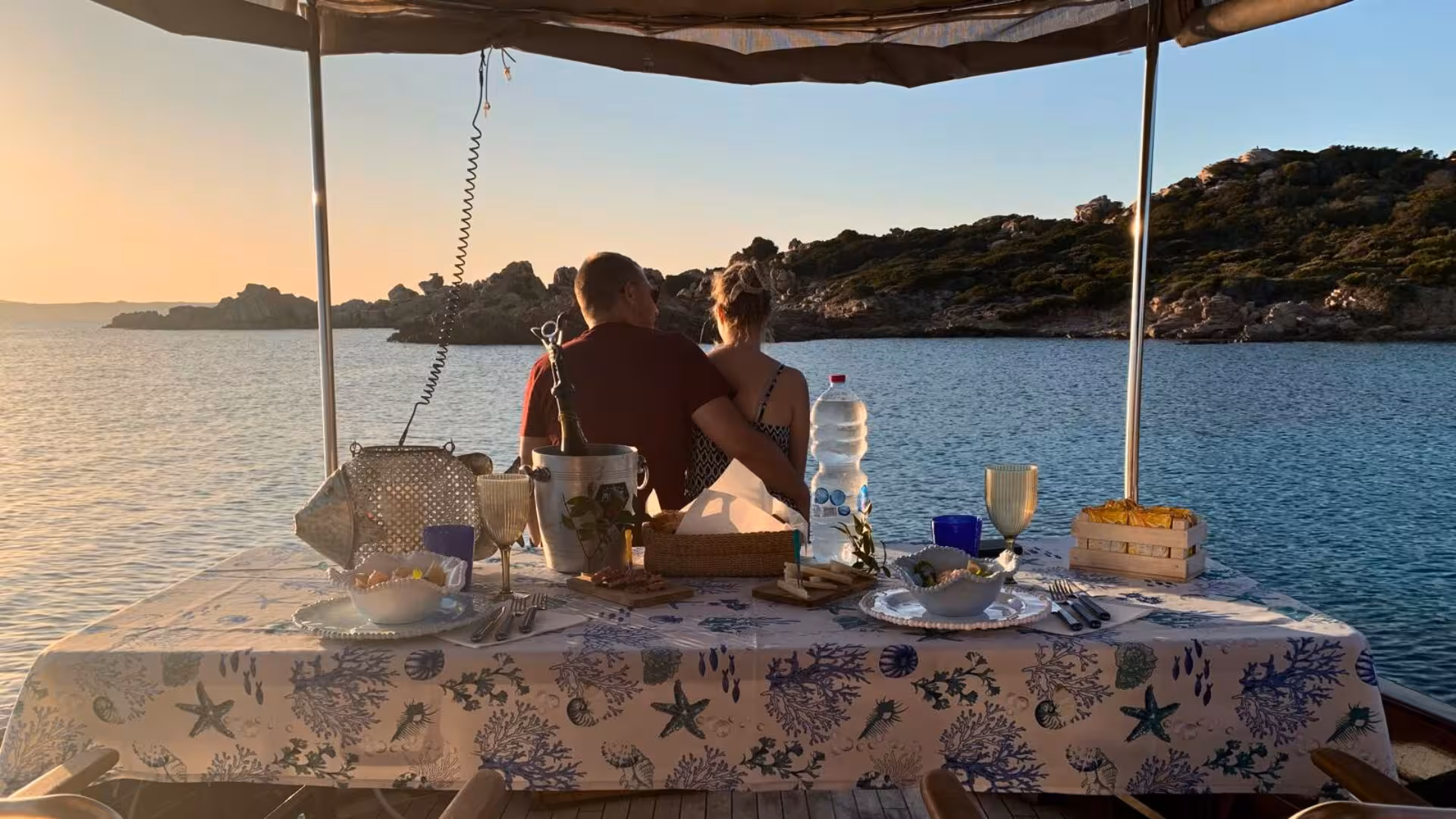 Couple enjoying a romantic sunset dinner on a boat tour in the La Maddalena Archipelago.