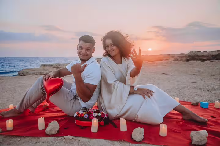 Couple enjoying a romantic beachside sunset photoshoot in Ayia Napa, surrounded by candles and holding a heart balloon.