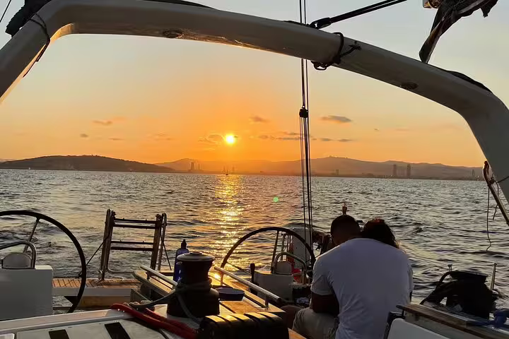 Couple enjoying a romantic sunset sailing experience with open bar and tapas, overlooking scenic ocean views and city skyline.