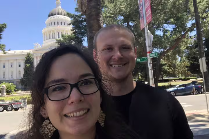 Smiling couple taking selfie in front of Sacramento State Capitol building on sunny day