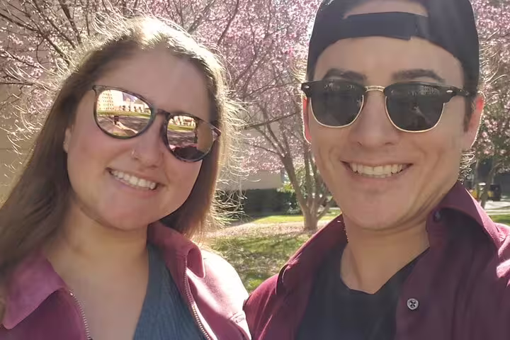 Smiling couple in sunglasses on romantic walking tour near cherry blossom trees in Sacramento