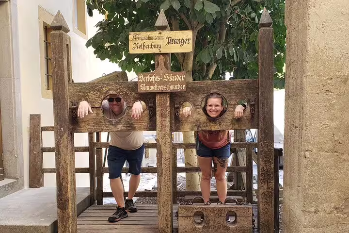 Couple posing in historic pillory on Rothenburg scavenger hunt, fun stop on self-guided Old Town tour