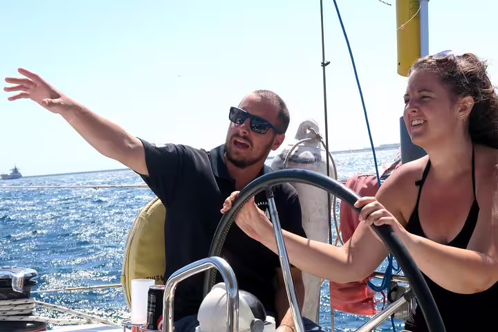 Couple enjoying a sunny 3-hour sailing trip with tapas and drinks, navigating the sparkling ocean under clear blue skies.