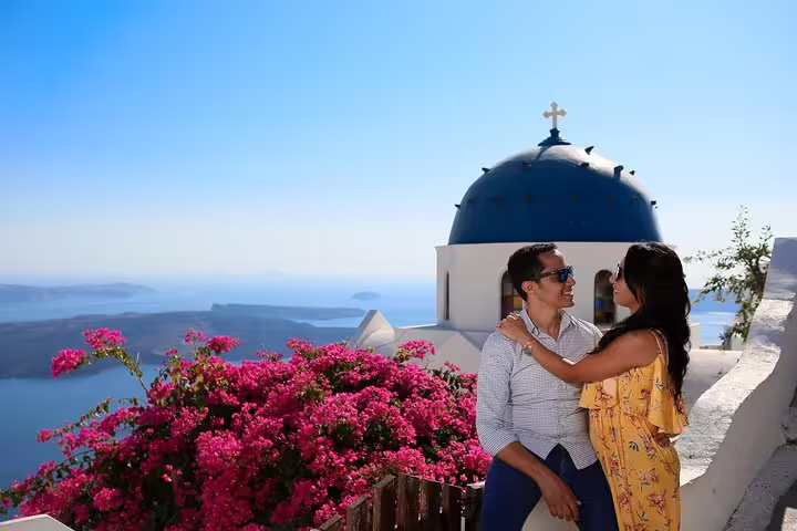 Couple enjoying scenic views of Santorini's blue-domed church with vibrant bougainvillea during a personal photographer tour.