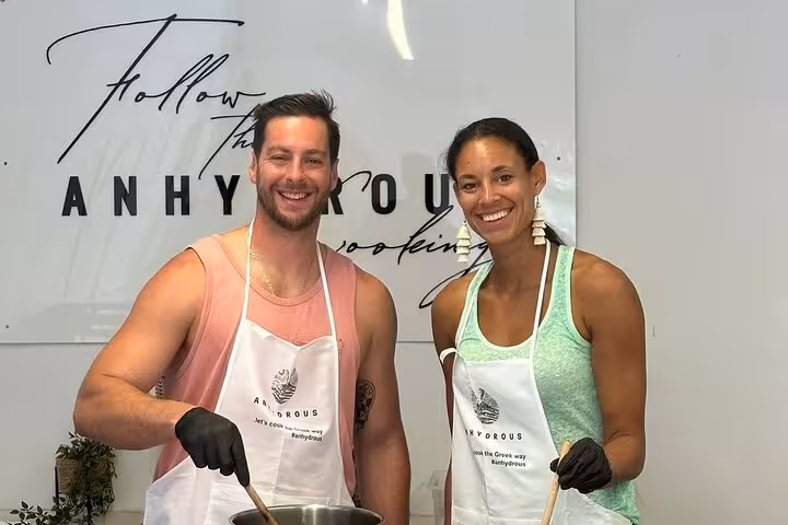 Happy couple in aprons stirring a pot at a Santorini private cooking class, part of an island tour