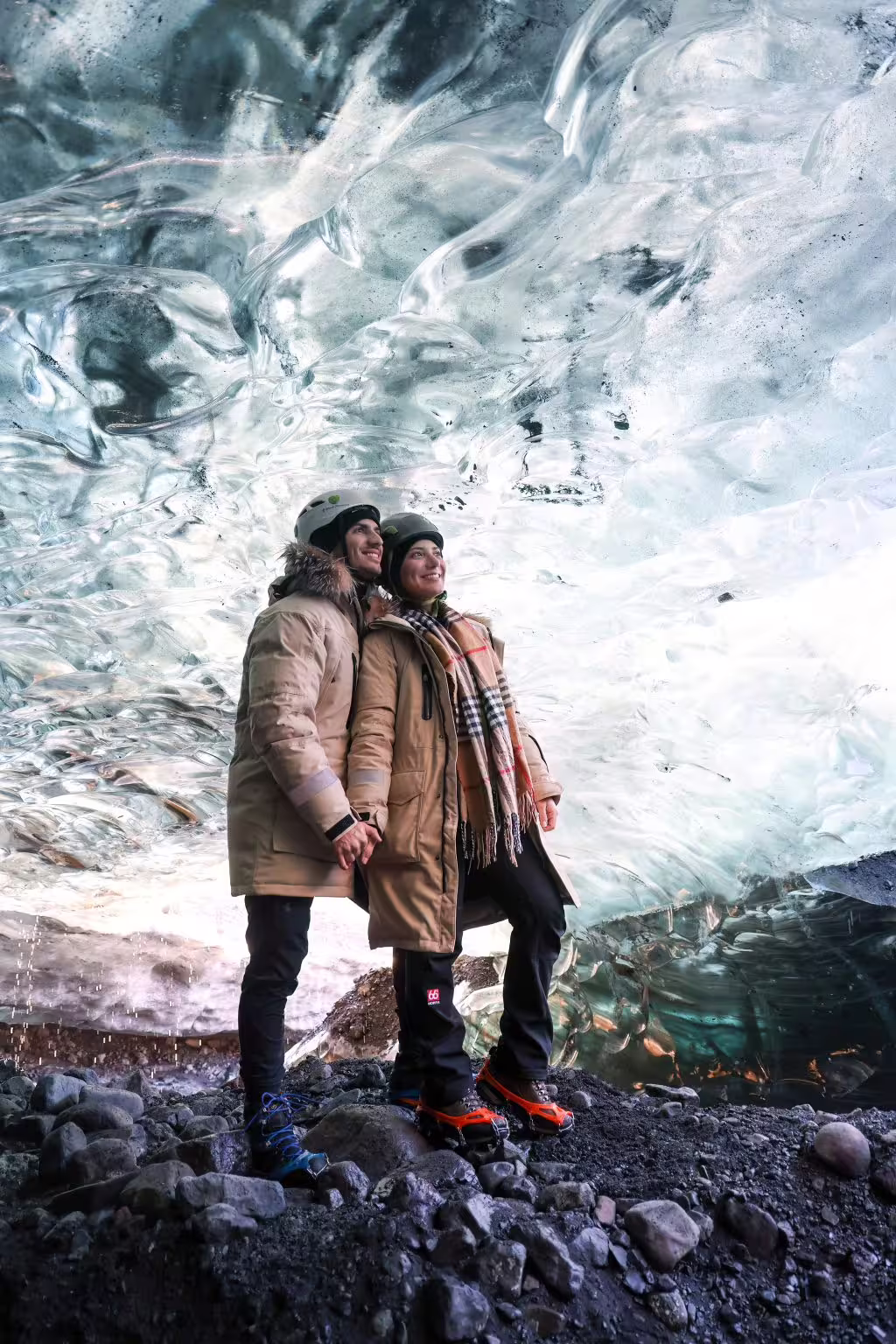 Smiling couple in winter gear and helmets stand inside a stunning sapphire ice cave on a guided Iceland glacier tour