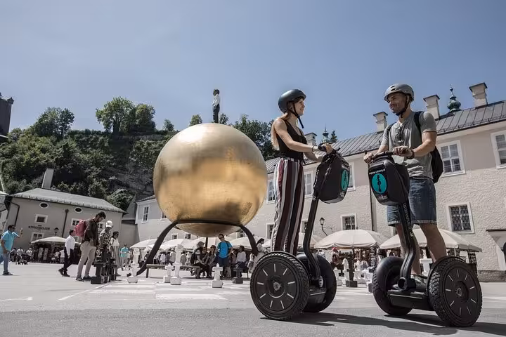Couple on Segways in Salzburg's Kapitelplatz, with the striking golden sphere sculpture in the background.