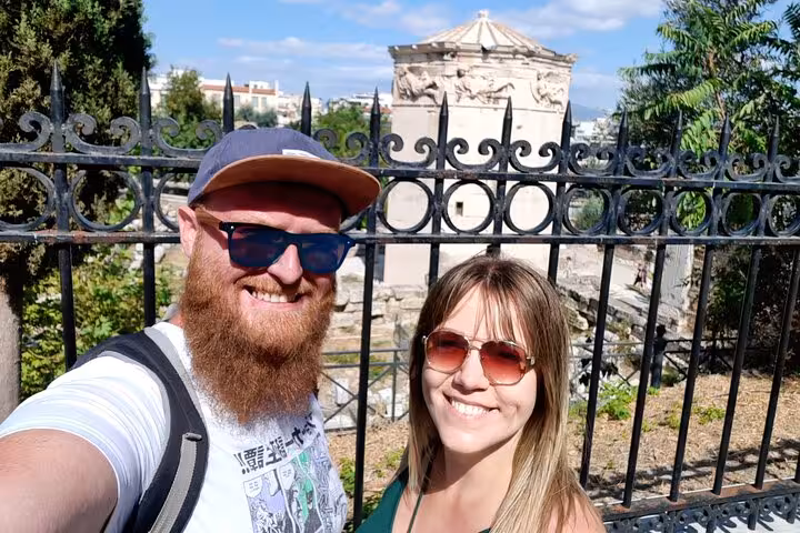 Couple taking selfie in front of ancient Greek ruins and ornate iron fence in Athens