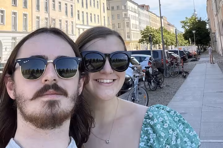 Couple wearing sunglasses taking a selfie on a Berlin street with parked bikes and classic buildings