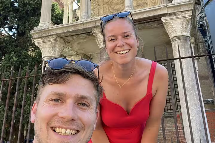 Smiling couple taking a selfie in front of an ornate historic stone monument in Bologna