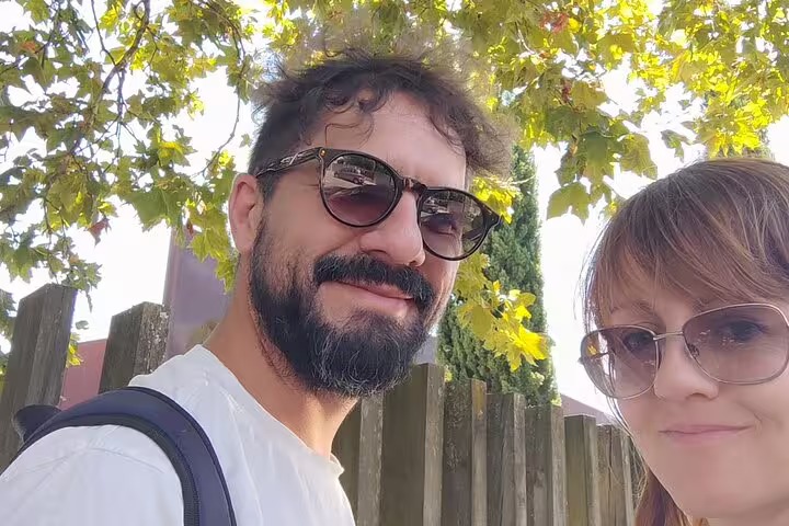 Couple taking a selfie outdoors near wooden fence and trees during walking tour in Braga