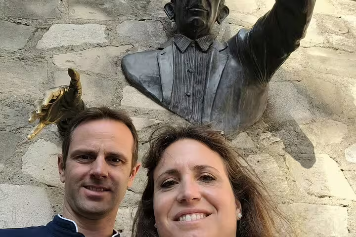 Couple taking selfie with bronze bust sculpture on stone wall in Montmartre Paris