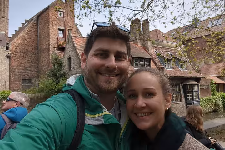 Couple taking a selfie on a canal walking tour in Bruges with historic brick buildings behind them