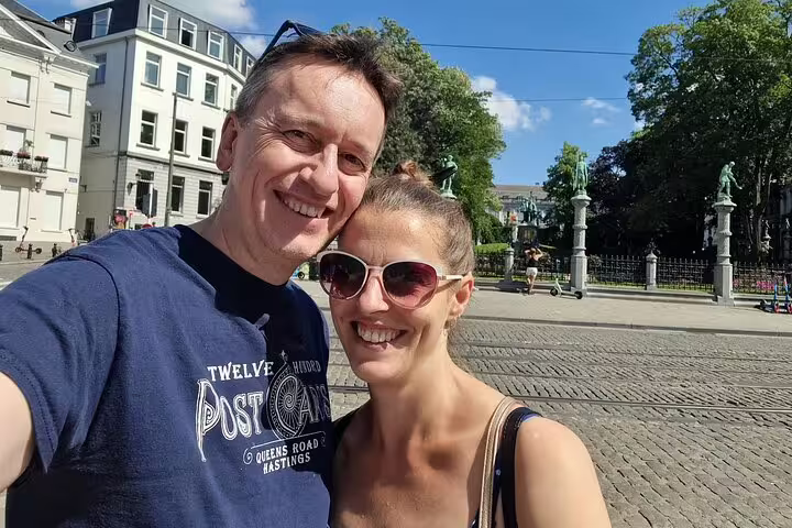 Smiling couple taking a selfie on a Brussels cobblestone square with statues and historic buildings
