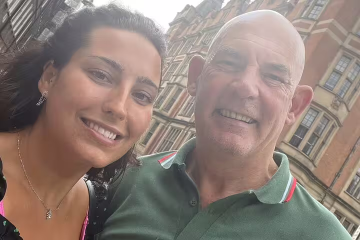 Smiling couple taking selfie on Charles Dickens walking tour in London with Victorian brick building behind