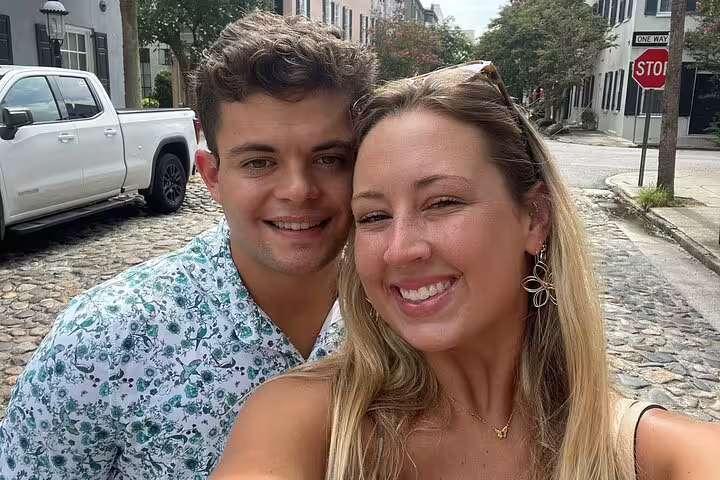 Smiling couple taking a selfie on a historic cobblestone street in Charleston, SC