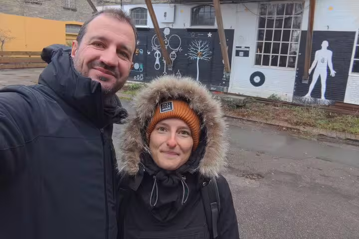 Couple smiling in selfie outside Christiania Copenhagen with street art murals in background