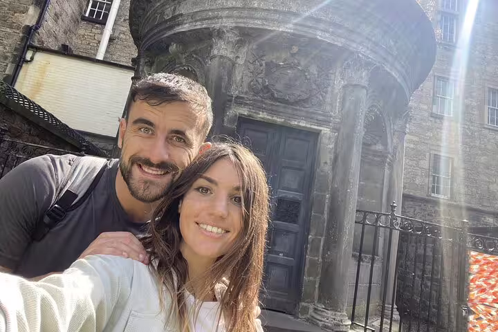 Couple smiling in selfie in front of ancient stone building on Edinburgh haunted walking tour