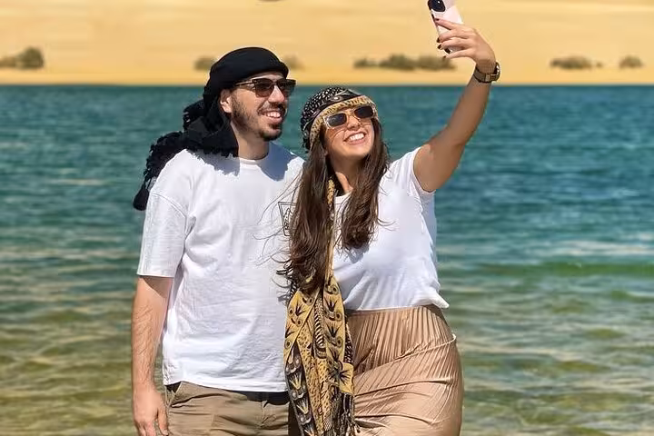 Couple taking selfie at Fayoum Magic Lake with sand dunes backdrop, Cairo to oasis tour experience