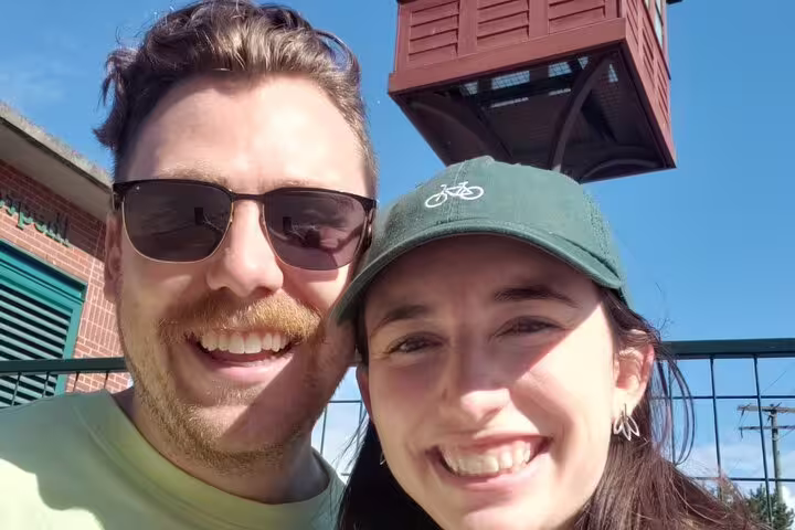 Smiling couple taking a selfie in Vancouver Gastown with a red historic tower in the background