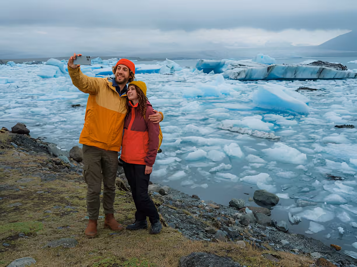 Couple taking selfie at Jökulsárlón glacier lagoon with blue icebergs on Iceland's South Coast