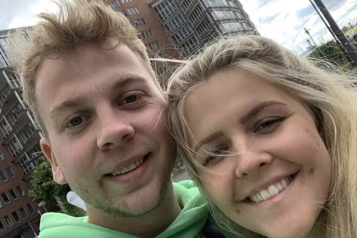 Smiling couple taking a selfie outdoors near Hamburg waterfront buildings on a cloudy day