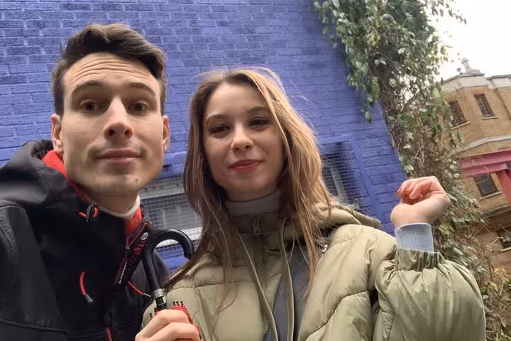 Couple taking a selfie during a self-guided walking tour near a blue brick wall in London