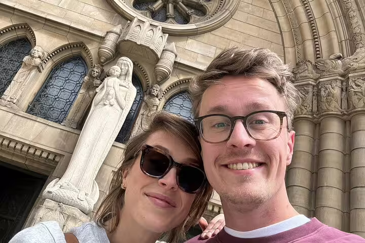 Couple smiling in selfie in front of ornate Luxembourg City cathedral with stone Madonna statue