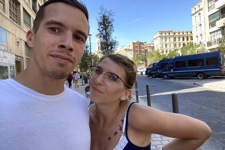 Couple taking selfie on a sunny street in Marseille Old Town with blue vans in background