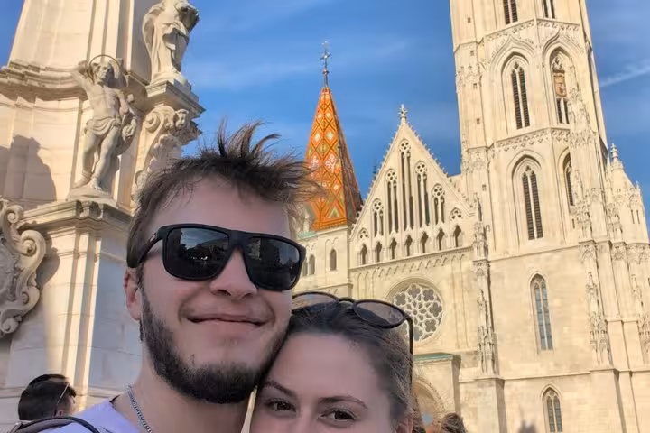 Couple taking selfie in front of Matthias Church with colorful tiled spire in Budapest Buda Castle