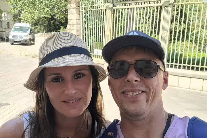 Couple taking a selfie on a sunny street in Montpellier near ornate iron gates