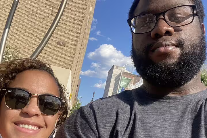 Two people taking a selfie outdoors in Philadelphia with city buildings and blue sky behind them.