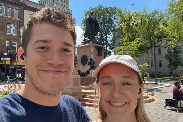 Couple smiling in front of a historic statue in Old Quebec City on a sunny day