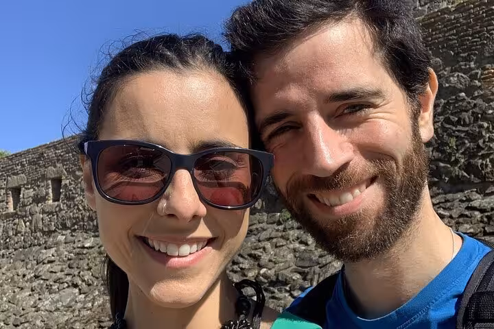 Smiling couple taking a selfie in front of ancient stone walls on a sunny day