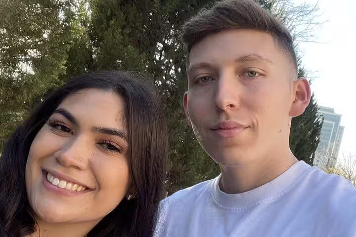 Smiling couple taking a selfie outdoors with trees in the background on a romantic walking tour