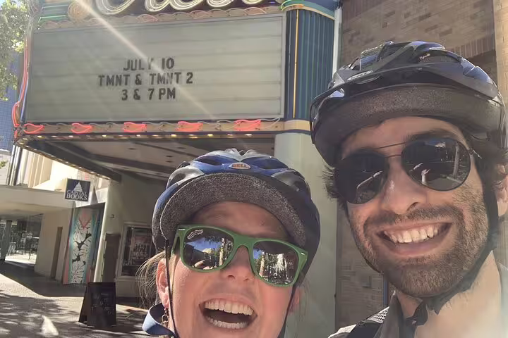 Couple in bike helmets and sunglasses smiling in front of Sacramento theater marquee