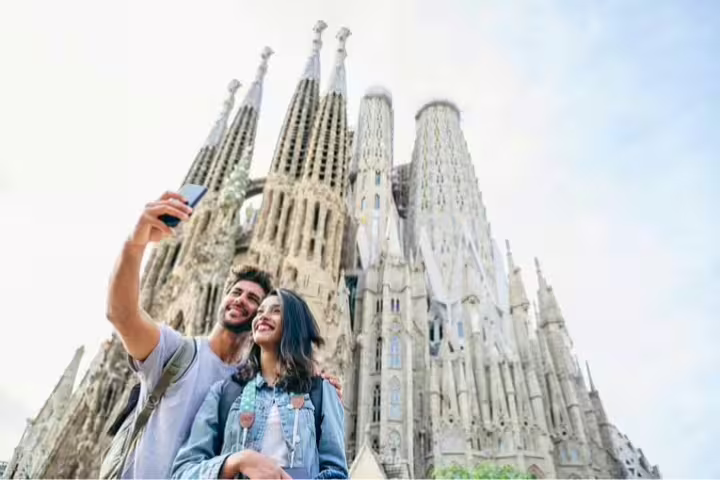 A couple takes a selfie in front of the iconic Sagrada Familia, capturing the essence of a private religious tour in Barcelona.