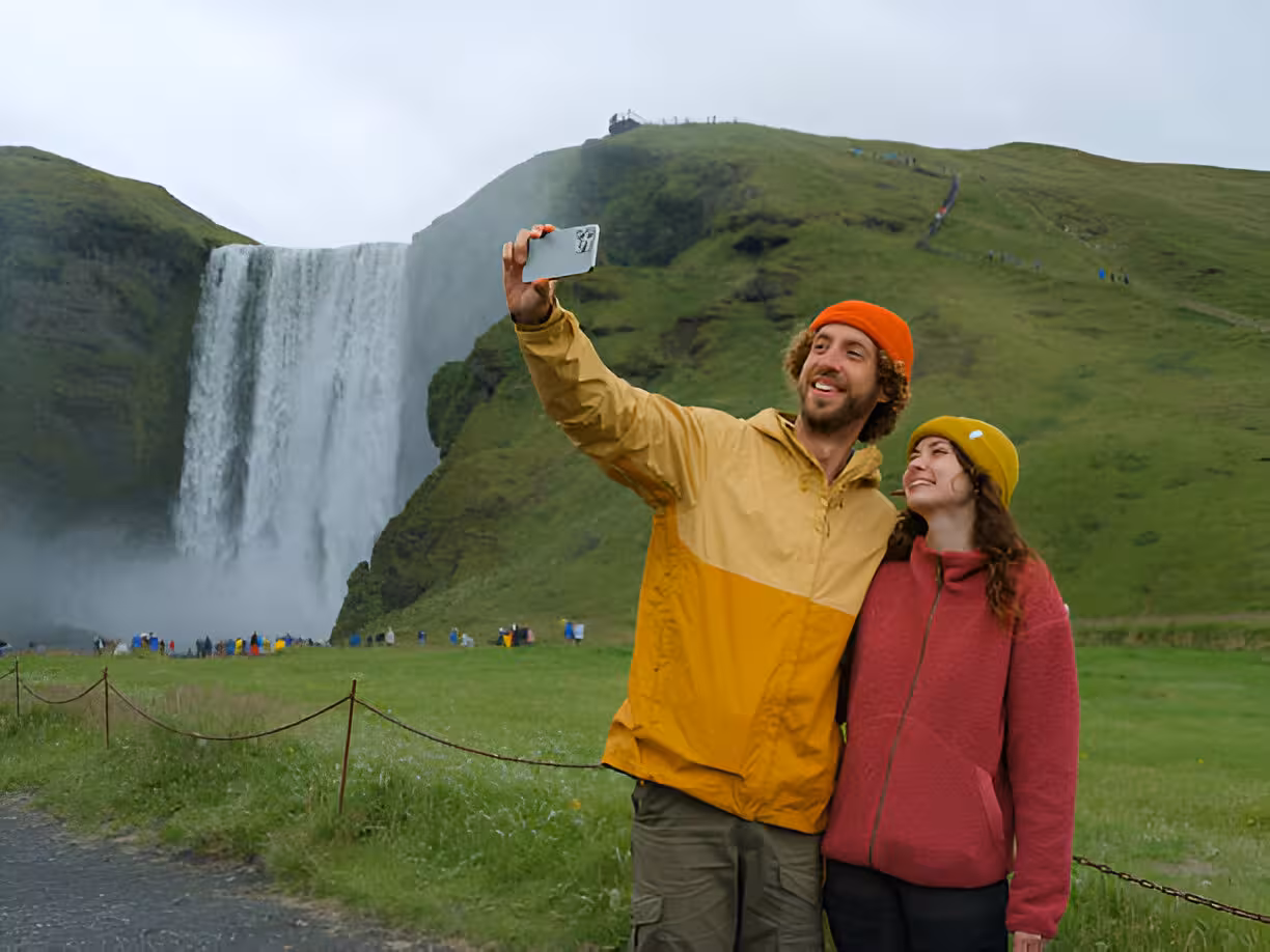 Couple taking selfie in front of Skógafoss waterfall on Iceland's green South Coast