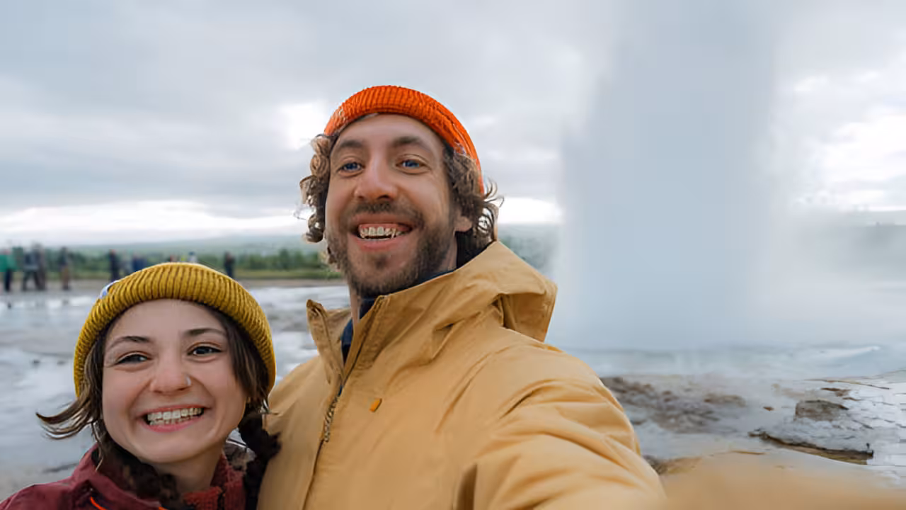 Couple smiling in selfie in front of erupting Strokkur geyser on Golden Circle Iceland tour